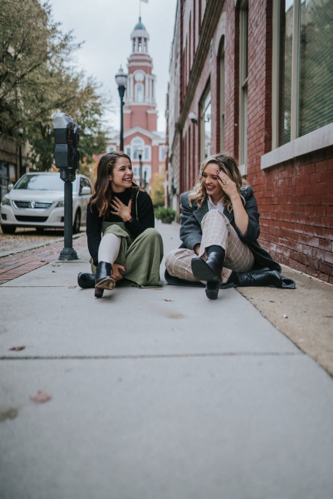 anna and celine laughing at joking sitting on the ground in downtown knoxville