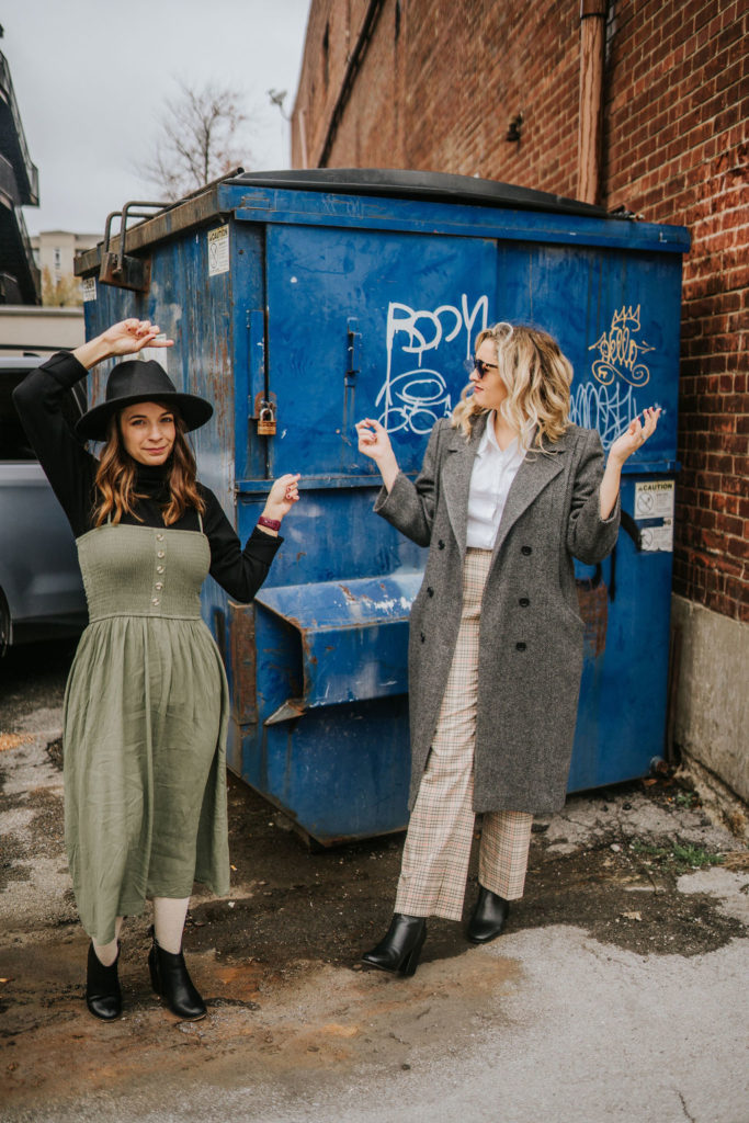 girl friends standing in front of dumpster pointing towards it