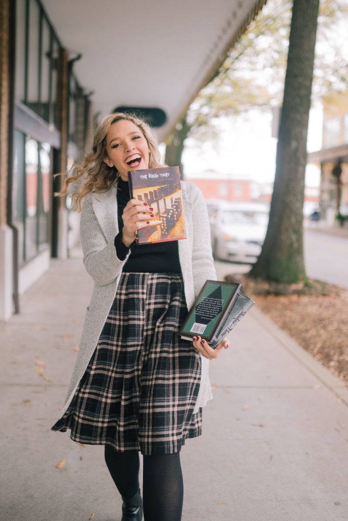 girl laughing holding stack of books on sidewalk
