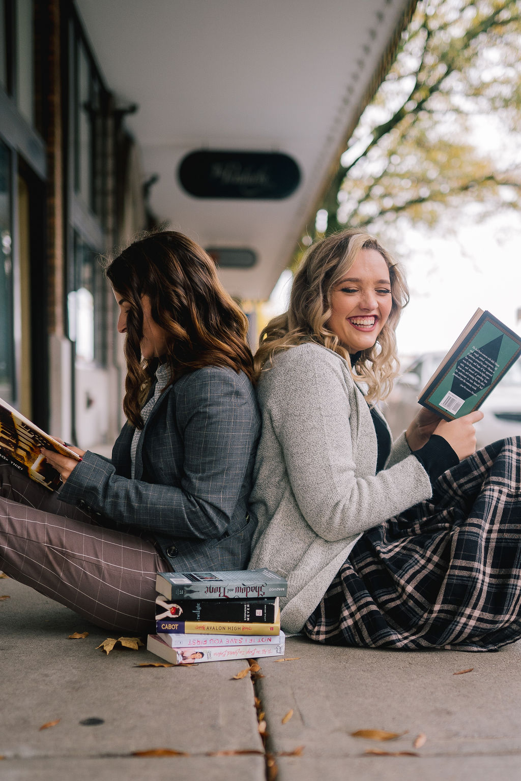 two girls back to back reading books and laughing